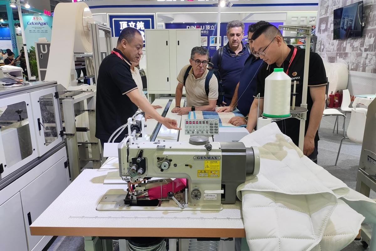 Customers closely examining both the quilting machine and various fabric samples at GENMAX’s CIFF Guangzhou exhibition booth.