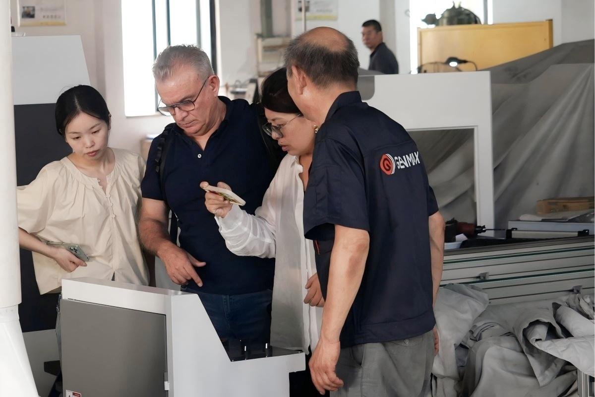 Textile industry professionals from Puebla, Mexico, observing the control system of a computerized multi-needle quilting machine as factory technicians explain its advanced operational features.