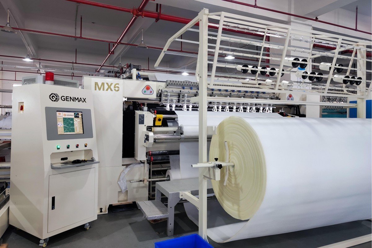 Front view of the Computerized Multi-Needle Quilting Machine showcasing the fabric feeding system and precision stitching components in the manufacturing facility