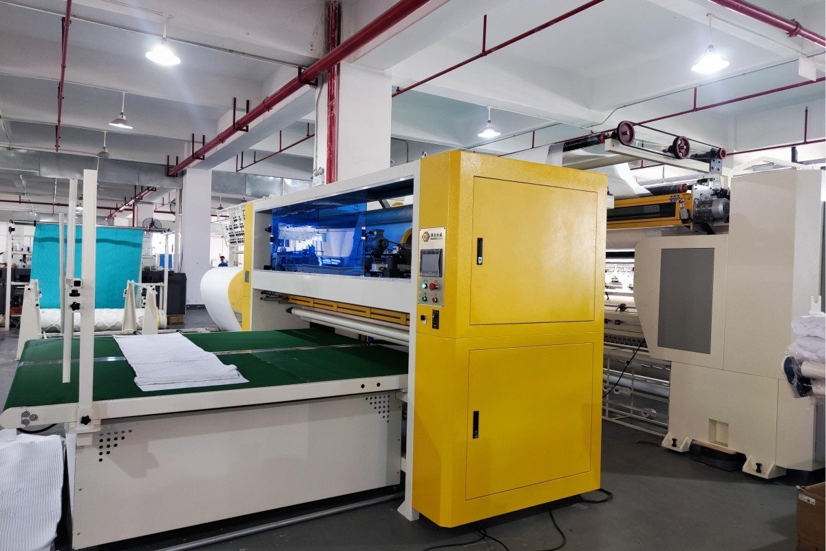 Rear perspective of an industrial quilting machine revealing the motor system, tension controls, and mechanical framework that powers the precision quilting operations for mattress productio