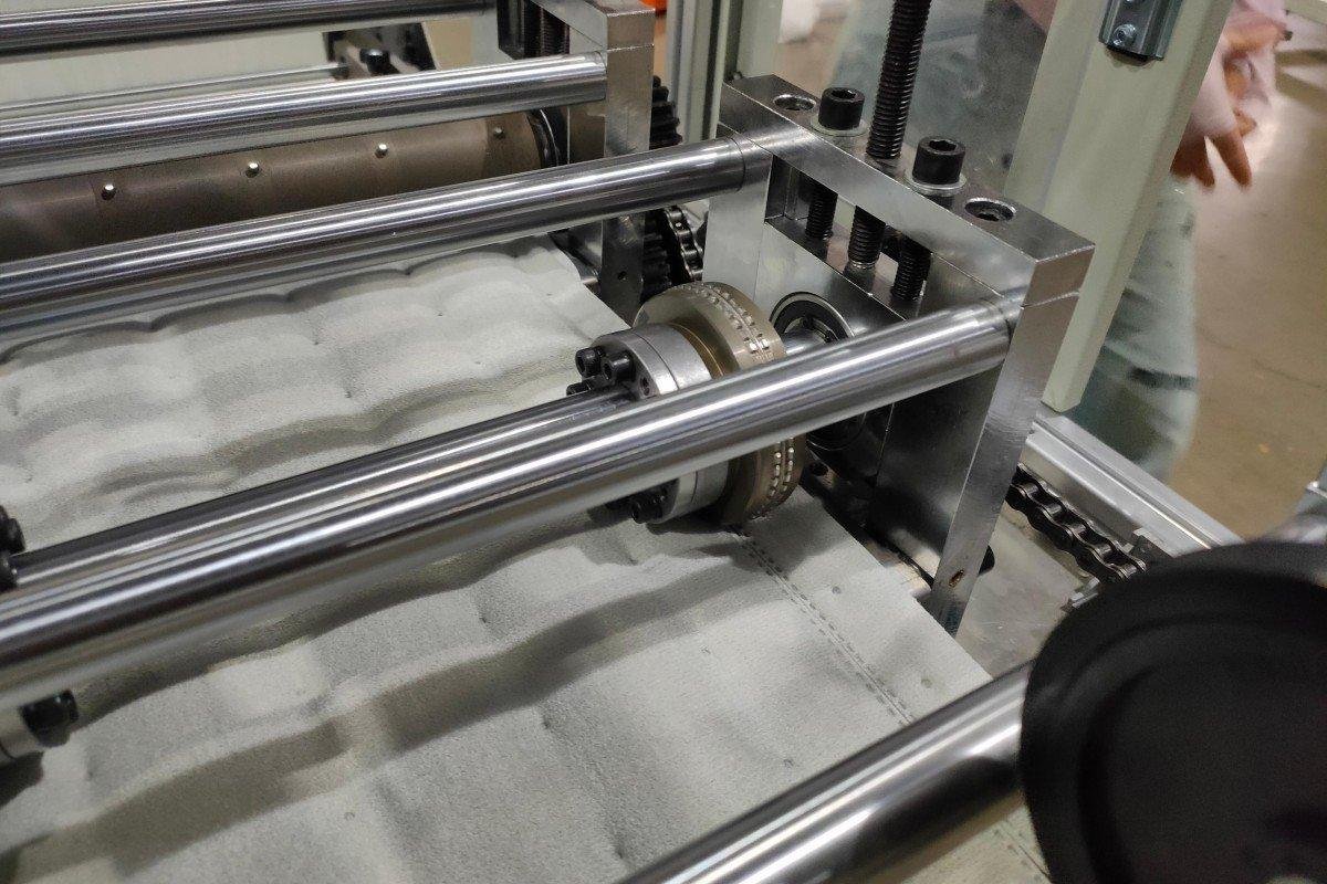 Small ultrasonic quilting machine in operation with samples of quilted textile products demonstrating the needle-free bonding technology for visiting customers.